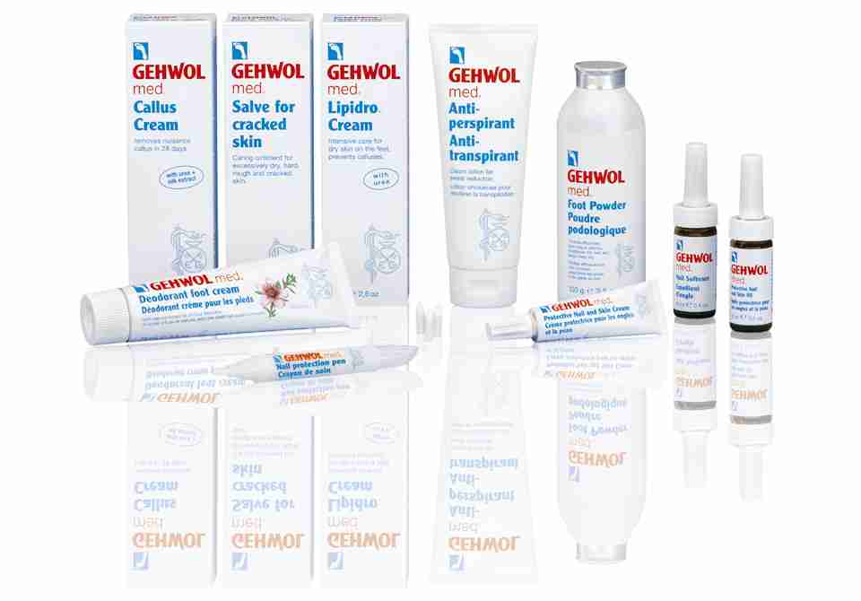 Sortiment av Gehwol fotvårdsprodukter, inklusive krämer, puder och sprayer, arrangerade på en vit reflekterande yta.